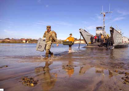 Corps Carry: Marine Corps Sgt. Evan Carlton carries equipment off a Navy utility landing craft during Steel Knight at Marine Corps Base Camp Pendleton, Calif., Dec. 2, 2023. The exercise is designed to train Marines in the planning, deployment and command and control of a joint force. USMC photo by Sgt. Anabel Abreu Rodriguez